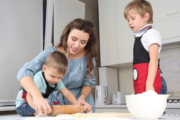 炊具妈妈帮小儿子在餐桌上揉面团准备厨师厨房