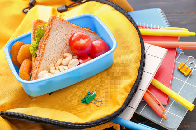 吃学校的饭盒和书包放在木头上三明治塑料水果