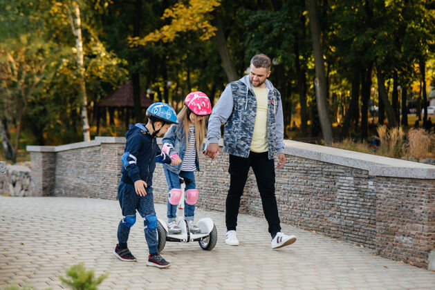 电力一位父亲帮助并教他的孩子在日落时分在公园里骑赛格威设备户外散步
