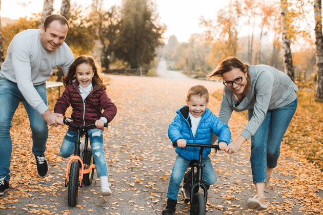 儿子年轻的父母帮助他们的孩子在公园里学骑自行车日落可爱女孩和她的哥哥正在学骑自行车自行车运动童年