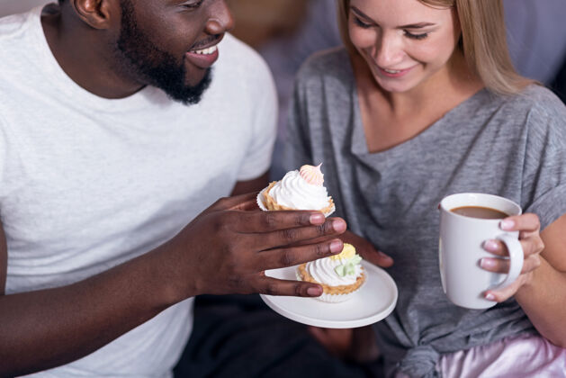 放松甜蜜的早餐很高兴国际年轻夫妇一边吃纸杯蛋糕 一边喝茶 一边享受早晨的时光享受舒适杯子