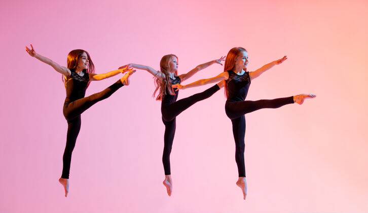青少年三个穿着黑色紧身套装的芭蕾舞女孩在红色背景上跳跃自信背景活动