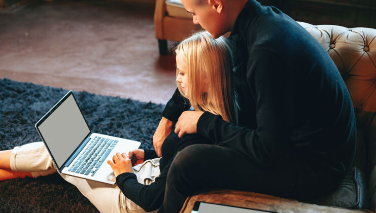 沙发一对可爱的夫妇在家里用电脑工作 在客厅里互相拥抱坐着科技金融