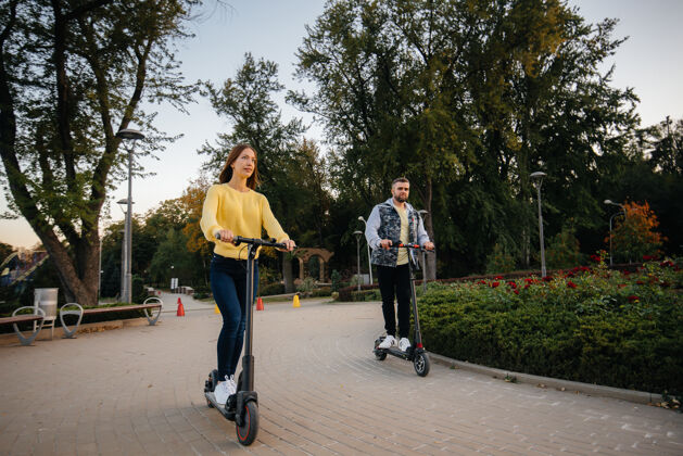 车辆在一个温暖的秋天 一对年轻漂亮的夫妇在公园里骑着电动滑板车户外女人环保