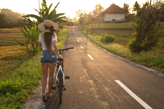 旅游年轻快乐的女人正骑着自行车走在狭窄的乡间小路上旅游夜晚运动