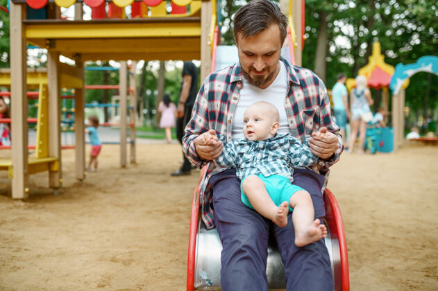 儿子快乐的父母和小宝宝在夏日公园的操场上玩耍放松夏天乐趣