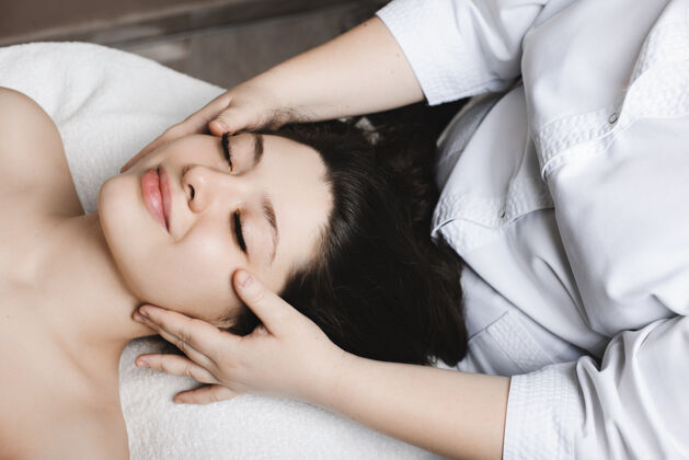 治疗一个神奇的女人斜倚在一张水疗床上 闭着眼睛 在一家健康水疗中心接受美容师的面部护肤治疗享受皮肤护理年轻