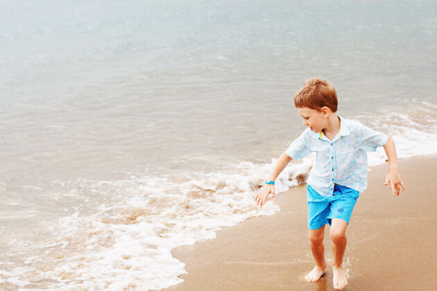 自然穿着衬衫和短裤的小男孩在沙滩上户外海岸微笑