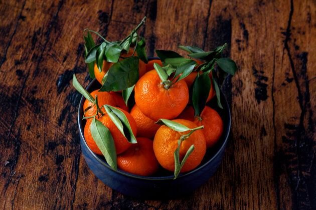 甜在一张旧木桌上 用蓝色陶瓷盘子盛着叶子的克莱门汀维生素橘子水果