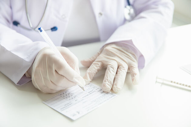 保健戴手套的医生的特写镜头填写冠状病毒疫苗接种护照 covid-19疫苗接种卡听诊器病毒流行病