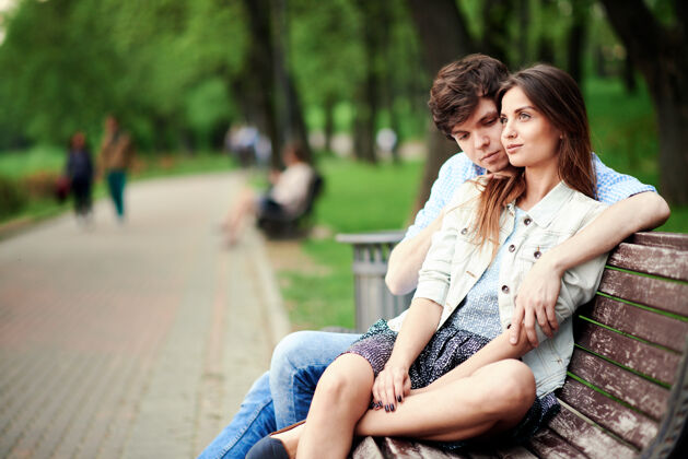 浪漫夏天 一个男人坐在公园的长椅上拥抱他的女朋友自然关系拥抱