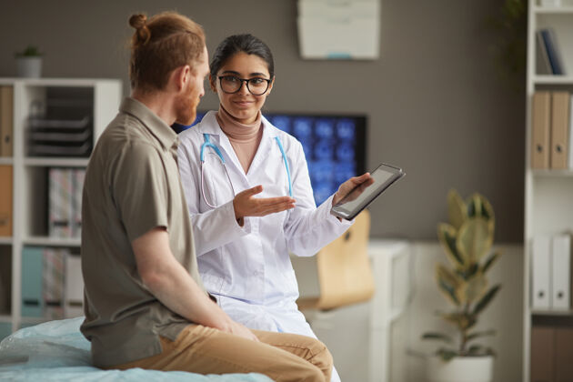 商务身穿白大褂的年轻护士在数字化平板电脑上展示药物配方 并在患者就诊期间与患者交谈休闲服访问职业
