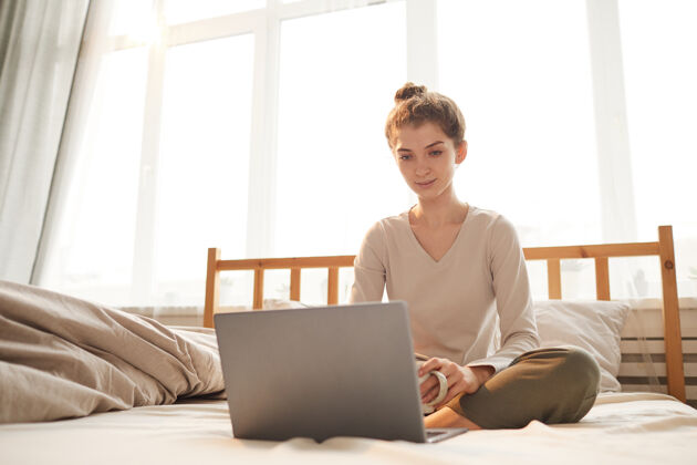 卧室照片中的年轻女子早上坐在卧室的床上看笔记本电脑的显示器房子美丽科技