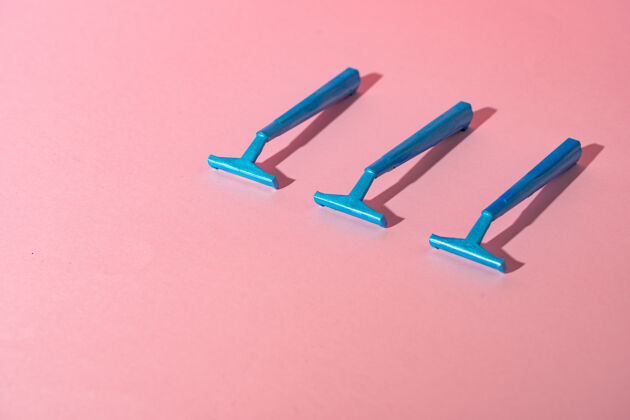 背景蓝色一次性剃须刀在粉红色的纸背景上卫生刀片切割