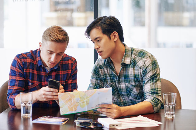 地图年轻人展示他在预订酒店时发现的不错的手机应用程序 手里拿着纸质地图给朋友亚洲人休闲装两个人
