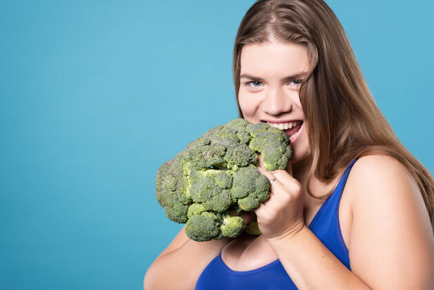 超大低碳水化合物肖像开心地笑着胖乎乎的女孩咬下花椰菜吃了食物特写减肥