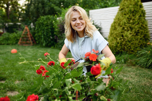 设备戴手套的快乐年轻女子在花园里和花一起工作花园女园丁照顾植物户外 园艺爱好 花店的生活方式和休闲人铲子勺子