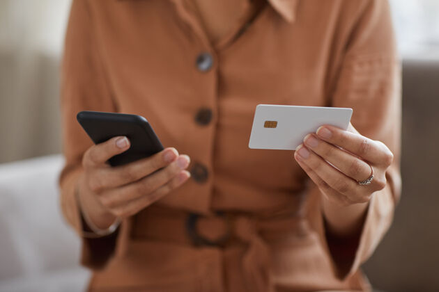室内特写镜头中 一个手里拿着手机和信用卡的女人在网上付账信息银行全球通信