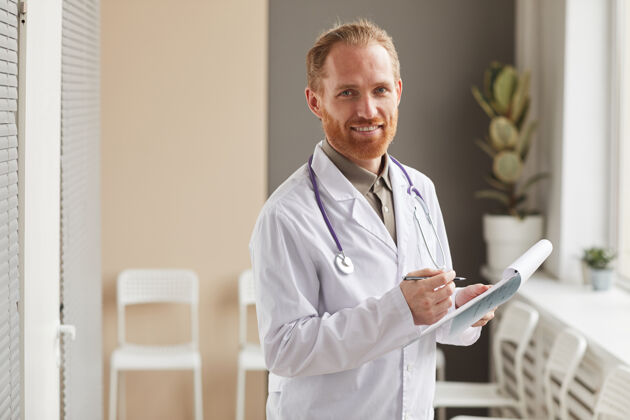 人站在医院走廊前 一位留着胡须 身穿白大褂 手持医疗卡 面带微笑的男医生的画像医疗职业听诊器医院