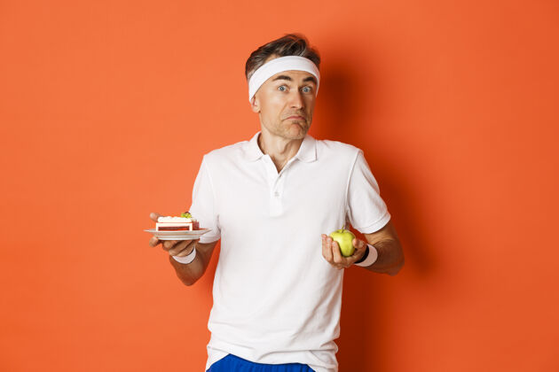 健身笨拙的中年健身者的画像 拿着苹果和蛋糕决定饮食蛋糕