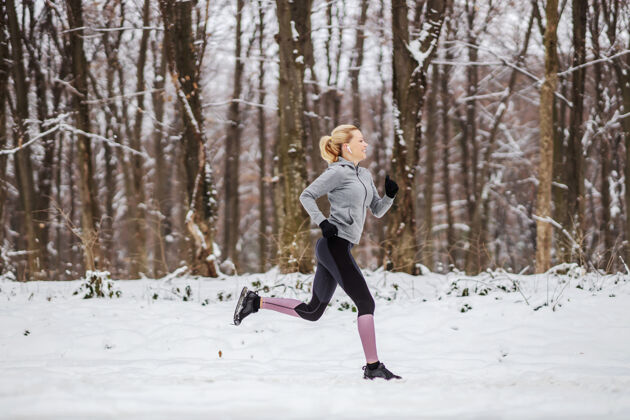 短跑在雪天的冬天 快跑的苗条女运动员在森林里奔跑白天比赛 自然慢跑 冬季健身私人教练寒冷成功
