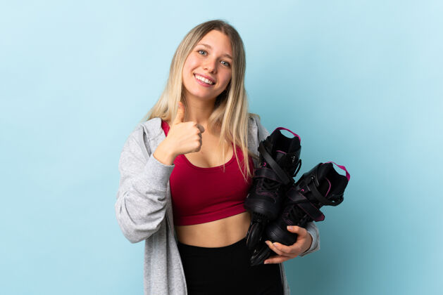 站立年轻的金发女子举着一只溜冰鞋孤零零地站在粉红色的墙上竖起大拇指Ok好微笑