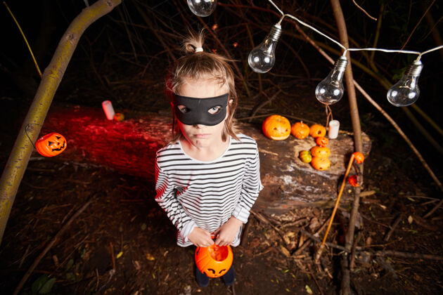 魔术万圣节派对上 戴面具的小女孩站在黑暗中和玩具南瓜的画像玩耍十月恐怖
