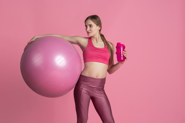 人美丽的年轻女运动员在粉色工作室墙上练习单色肖像女性锻炼一