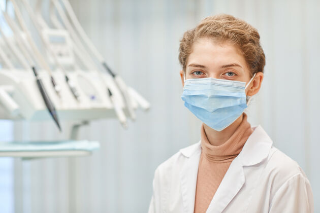 牙医办公室戴着防护面具的年轻女牙医站在牙科诊所前面的画像外科口罩防护服自信