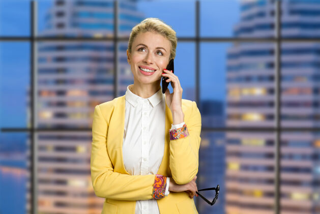 肖像微笑的商务女士拿着电话快乐的年轻女子在晚间商务中心用手机交谈成人手机个人