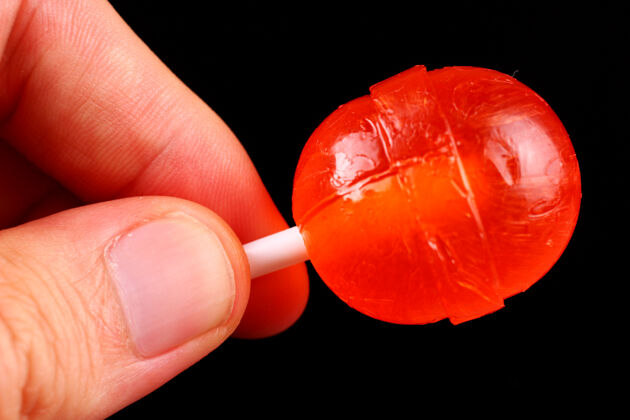 棒手里拿着红糖 粘在黑色的表面上对待糖果颜色