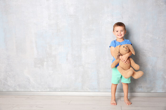 天真可爱的小男孩和玩具兔子靠近灰墙站肖像光