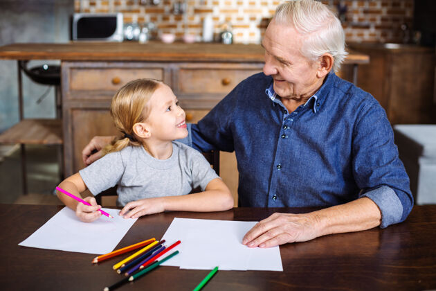 坐着快乐的小女孩坐在桌子边和爷爷一起画画欢呼孩子快乐