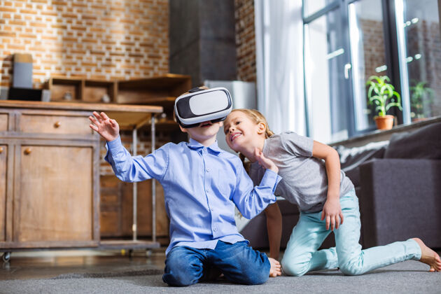 科技快乐的小男孩坐在地板上和他的妹妹 而使用虚拟现实眼镜耳机孩子现代