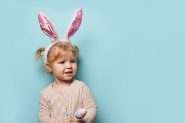 童年一个可爱的小女孩穿着复活节兔子耳朵拿着彩蛋在蓝色表面的肖像快乐欢笑兔子