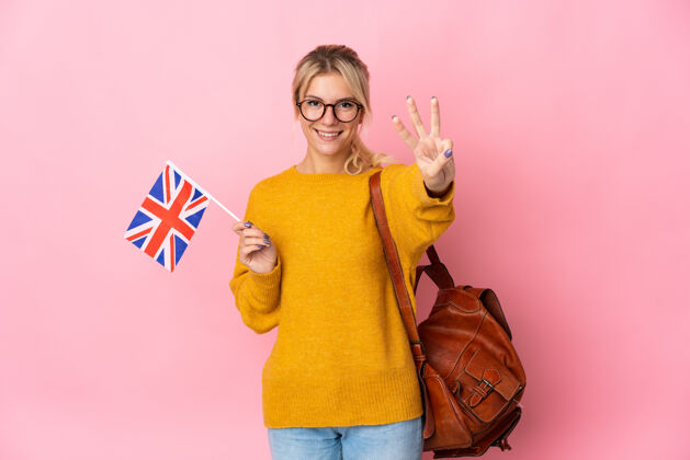成功一位年轻的俄罗斯妇女手持英国国旗 在粉红色背景上快乐地数着三个手指手3青年