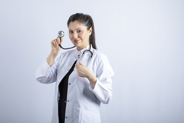 医疗保健穿着白大褂的漂亮医生站在白墙上 摆姿势制服自信女人