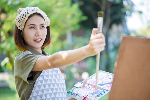 女士亚洲美女在夏日的田野里拿着画笔测量着纸艺板的距离绘画自然休闲