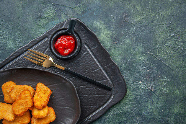 盘子在黑色盘子上放半张鸡块 在深色托盘上叉上番茄酱食物饭菜子弹