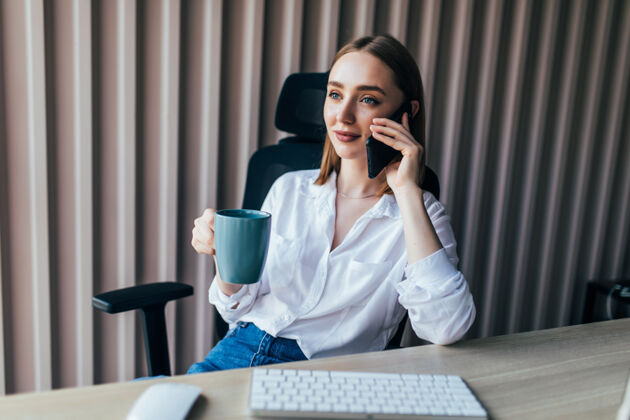 企業家在咖啡杯旁的辦公桌上 一位可愛的年輕女士一邊用手提電腦一邊打電話商務女性在線咨詢