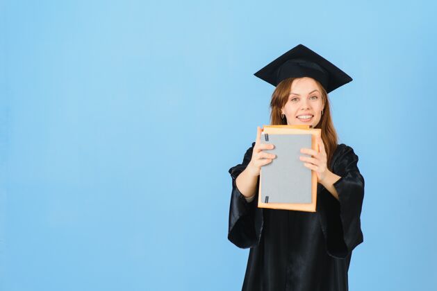 女性戴着毕业帽和毕业礼服的女研究生 背景是蓝色的学士享受成就