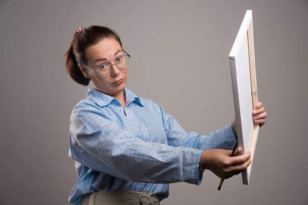 画笔戴着眼镜的女人拿着画布 在灰色上画笔高质量的照片女眼镜女