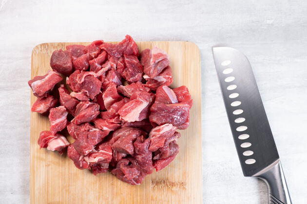 产品把生牛肉切成块放在桌上的木板上膳食肉刀