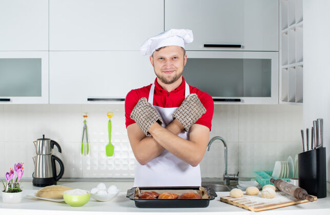 帽子俯视图：面带微笑的男厨师戴着支架站在桌子后面 上面放着糕点鸡蛋刨子 在白色的厨房里做着停下来的手势视图人淋浴帽