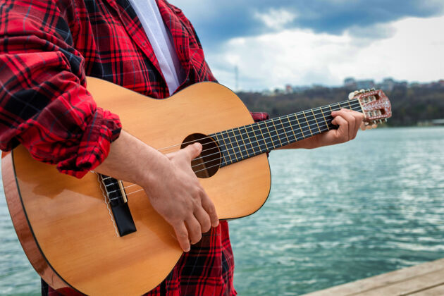 城市穿红衫的年轻人在公园的湖边弹吉他男人夏天红衫