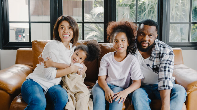 非洲快乐的非洲裔美国家庭 爸爸 妈妈和女儿在家里沙发上的笔记本电脑上享受着快乐的拥抱和视频通话放松视频通话女人