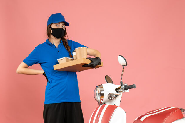 抱俯视图疲惫的快递员女孩戴着医用口罩手套站在摩托车旁拿着咖啡小蛋糕上粉彩的桃色摩托车立场高尔夫