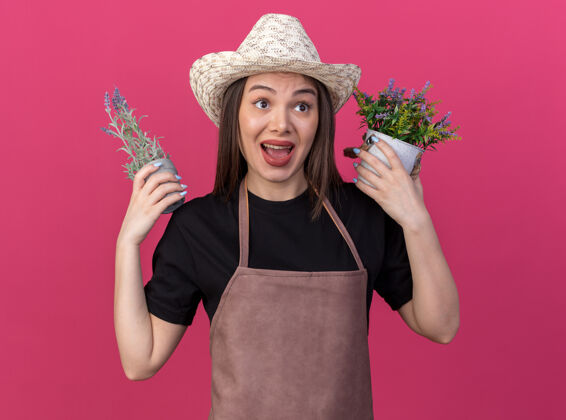粉红色焦急美丽的白人女园丁戴着园艺帽手持花盆望着身边穿园艺帽子