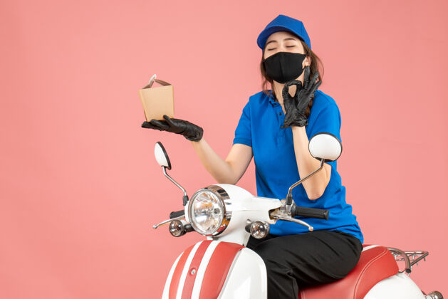 手套上图：戴着医用面罩和手套的快乐送货人坐在滑板车上 在柔和的桃色背景下送货滑板车摩托车送