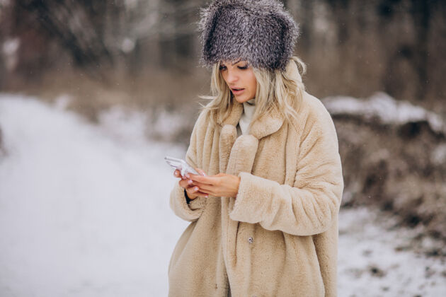女性穿着冬衣的女人走在满是雪的公园里打电话户外公园休闲